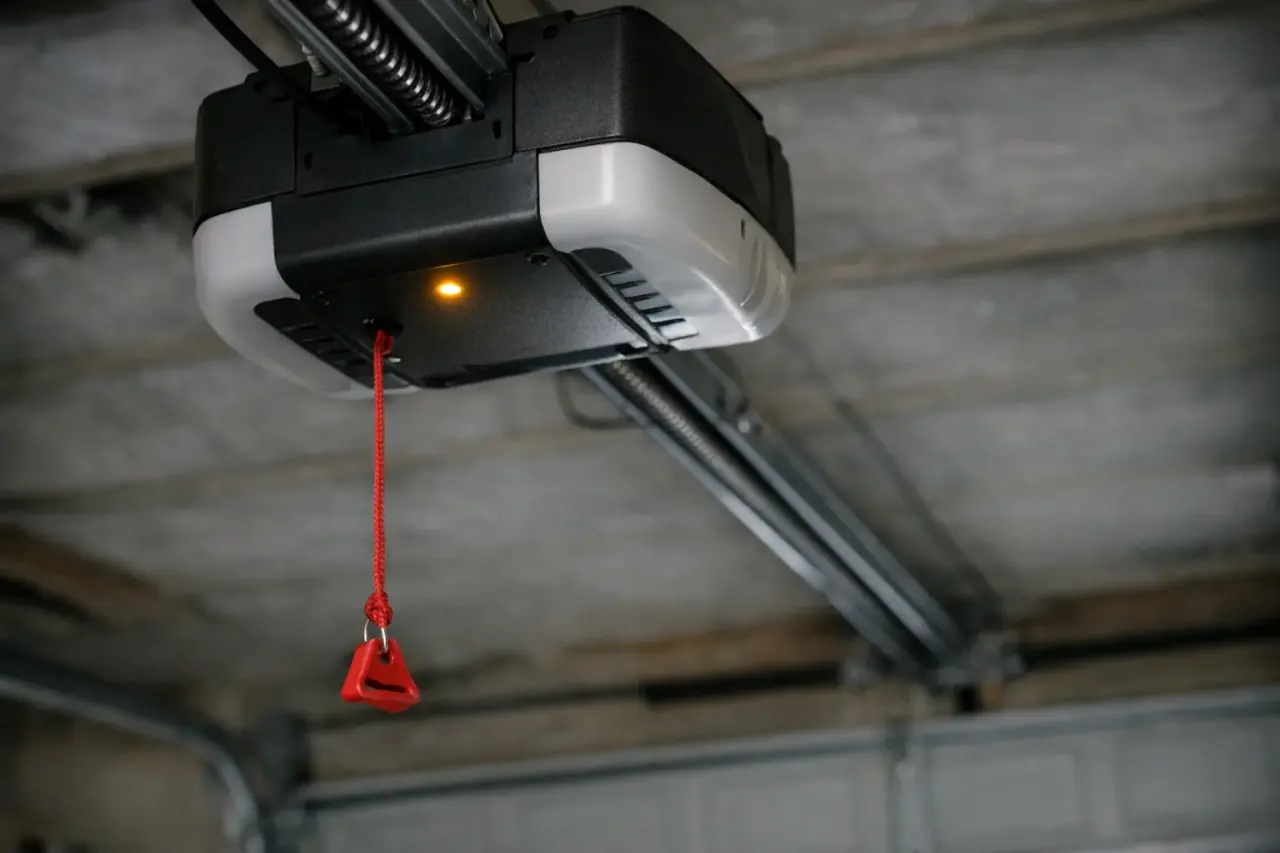 Ceiling-mounted garage door opener powerhead with a glowing status light and a red emergency release cord