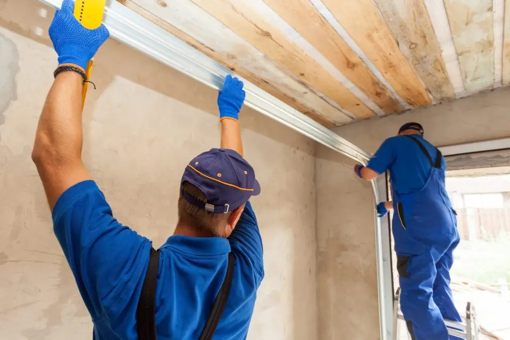 How to Winterize Your Home with Garage Door Insulation Two technicians installing or adjusting vertical garage door tracks in residential garage